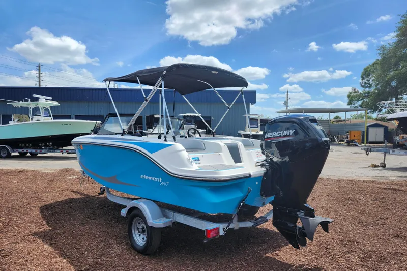 Slide: The Image of 2023 Bayliner Element M17 boat with Mercury engine, parked outdoors under a blue sky. - 5