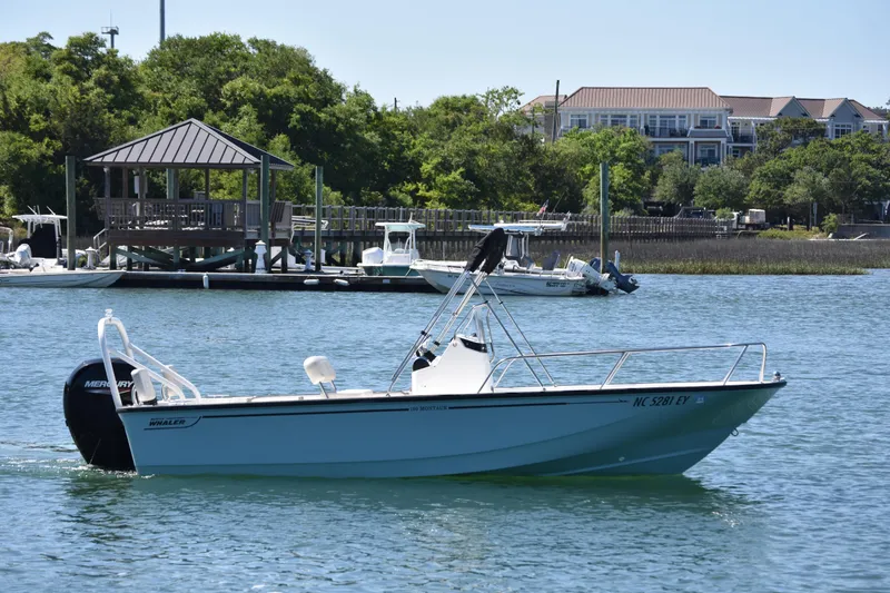 The Image of 2022 Boston Whaler 190 Montauk boat cruising on a scenic waterfront with docks and greenery. - 1