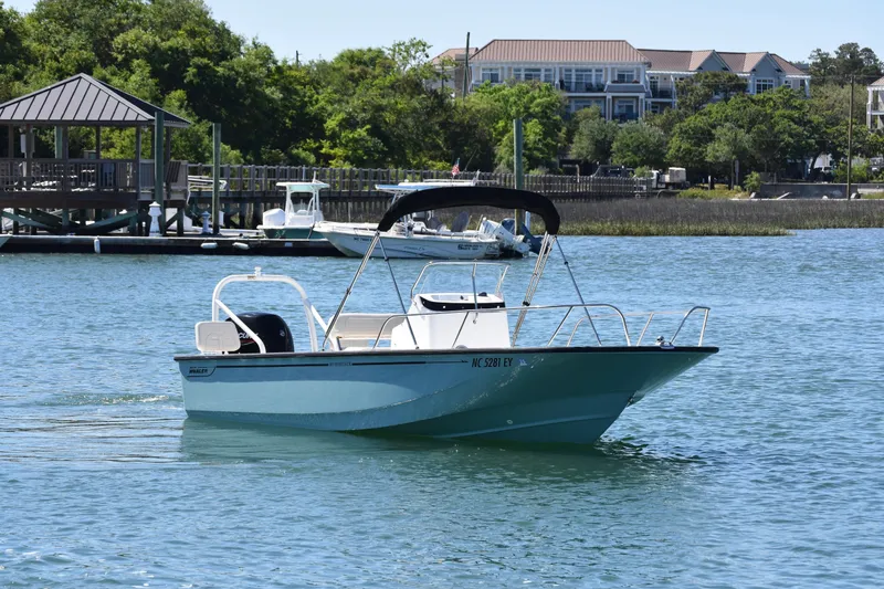 Slide: The Image of 2022 Boston Whaler 190 Montauk boat cruising on a scenic waterfront with docks and greenery. - 3