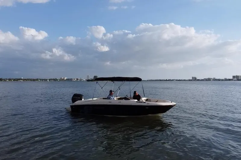 Slide: The Image of 2019 Bayliner Element E18 boat cruising on a calm lake under a partly cloudy sky. - 18
