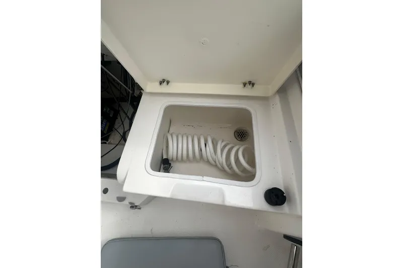 Slide: The Image of 2023 NAUTIC STAR 22 L boat compartment with coiled hose and drainage. - 13