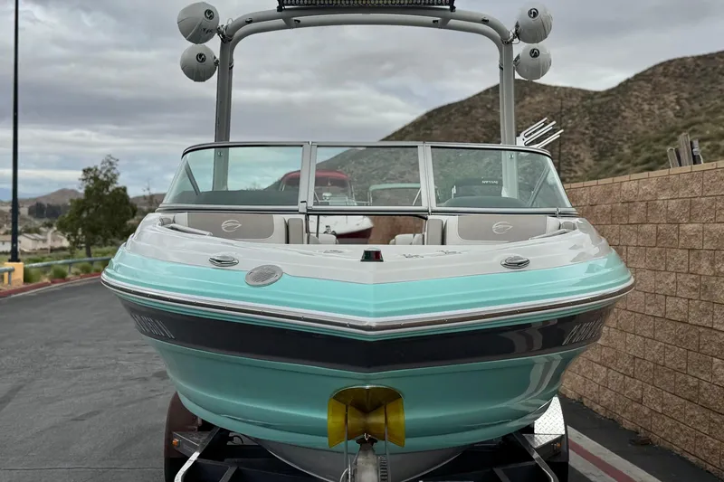 Slide: The Image of 2022 Crownline 220 SS SURF boat with turquoise hull, parked on a trailer. - 2