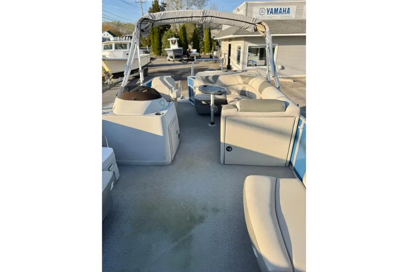 Slide: The Image of 2018 Starcraft EX 22 C SG pontoon boat with beige seating and canopy, parked near Yamaha dealership. - 22