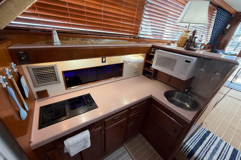 Slide: The Image of 1986 Bertram 46 Convertible yacht kitchen with stove, microwave, sink, and wooden cabinetry. - 16