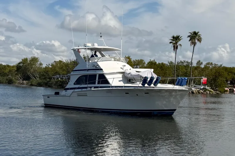 Slide: The Image of 1986 Bertram 46 Convertible yacht cruising on a calm waterway with palm trees in the background. - 2