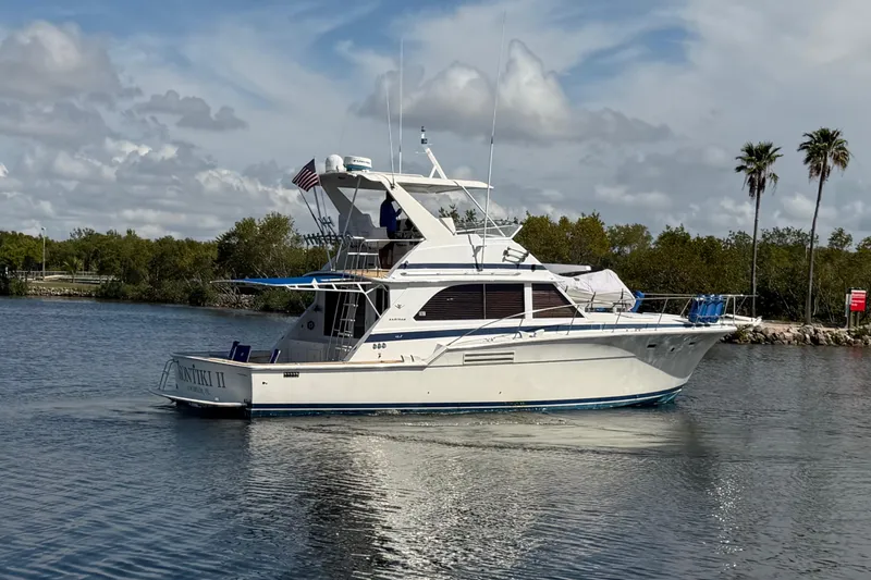 Slide: The Image of 1986 Bertram 46 Convertible yacht cruising on a calm waterway under a partly cloudy sky. - 5