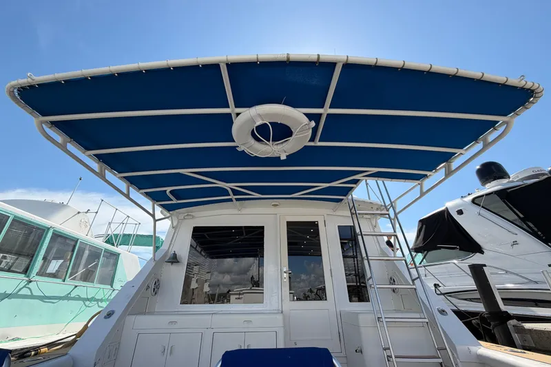 Slide: The Image of 1986 Bertram 46 Convertible yacht with blue canopy and lifebuoy, docked under clear sky. - 52