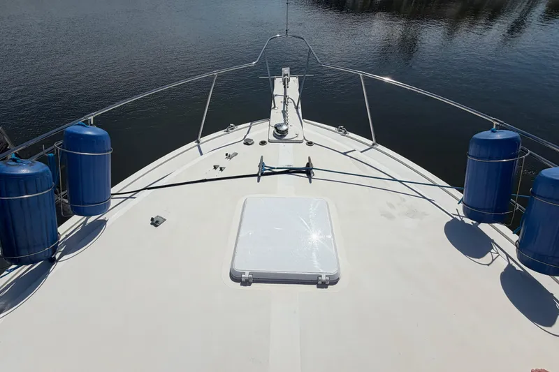 Slide: The Image of Bow view of 1986 Bertram 46 Convertible yacht with blue fenders on calm water. - 61