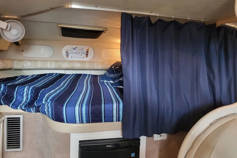 Slide: The Image of 1999 Rinker Fiesta Vee 330 cabin interior with blue-striped bedding and dark curtains. - 17