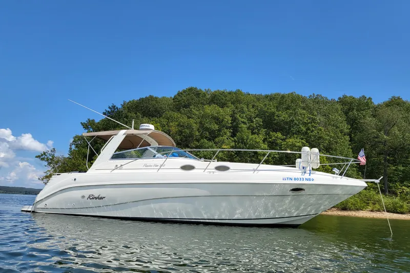 Slide: The Image of 1999 Rinker Fiesta Vee 330 boat on a serene lake with lush green forest backdrop. - 2