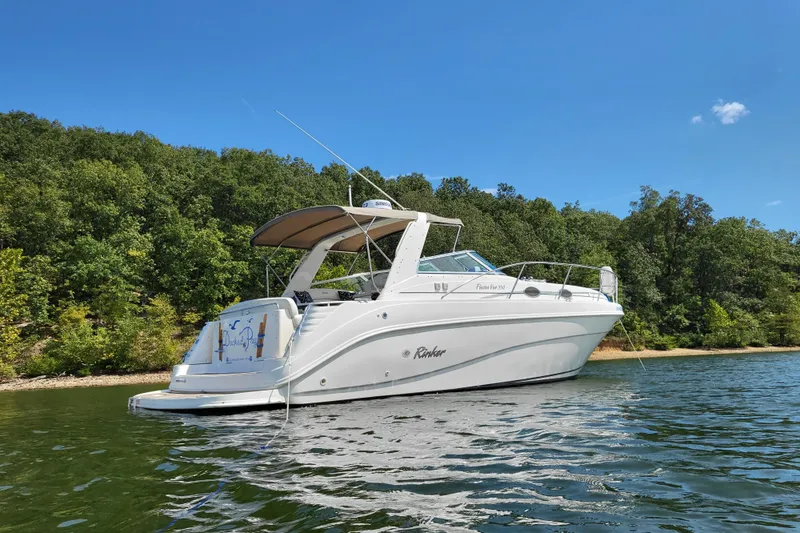 Slide: The Image of 1999 Rinker Fiesta Vee 330 boat on a serene lake with lush green forest backdrop. - 5