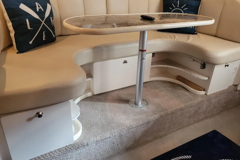 Slide: The Image of 1999 Rinker Fiesta Vee 330 interior with beige seating and table, featuring nautical-themed pillows. - 6