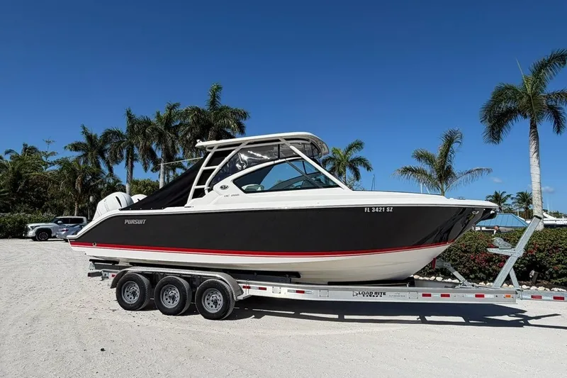 The Image of 2021 Pursuit DC 266 Dual Console boat on trailer, parked near palm trees. - 0