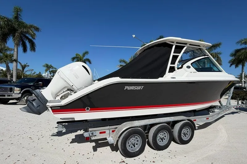 Slide: The Image of 2021 Pursuit DC 266 Dual Console boat on trailer, parked under clear blue sky. - 2