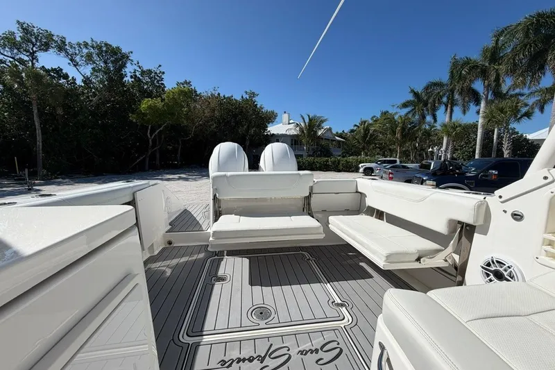 Slide: The Image of 2021 Pursuit DC 266 Dual Console boat interior with seating, parked near palm trees. - 5