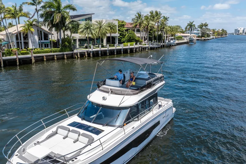 Slide: The Image of 2024 Jeanneau NC 1295 Fly yacht cruising near waterfront homes and palm trees. - 14