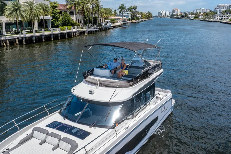 Slide: The Image of 2024 Jeanneau NC 1295 Fly yacht cruising on a scenic waterway with palm trees. - 16