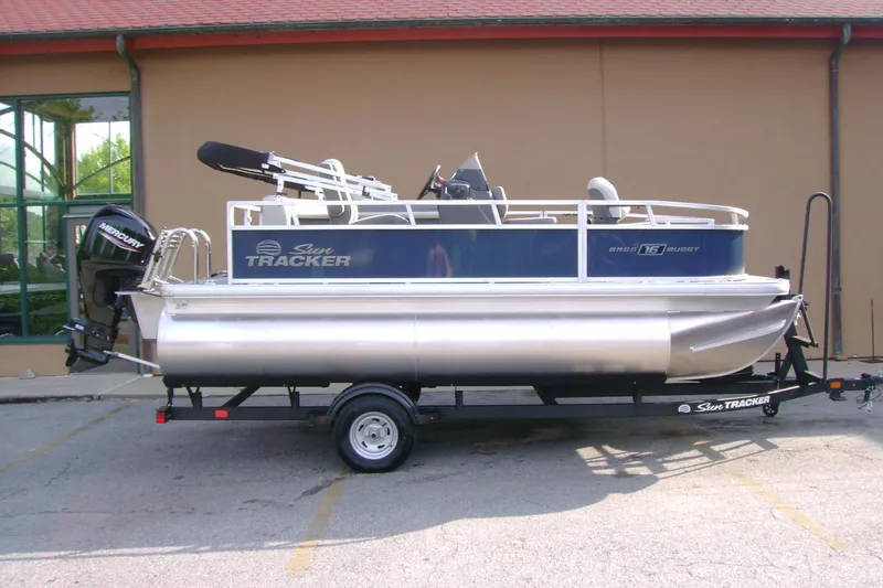 The Image of 2026 Sun Tracker Bass Buggy 16 XL Select pontoon boat on trailer, parked outdoors. - 0
