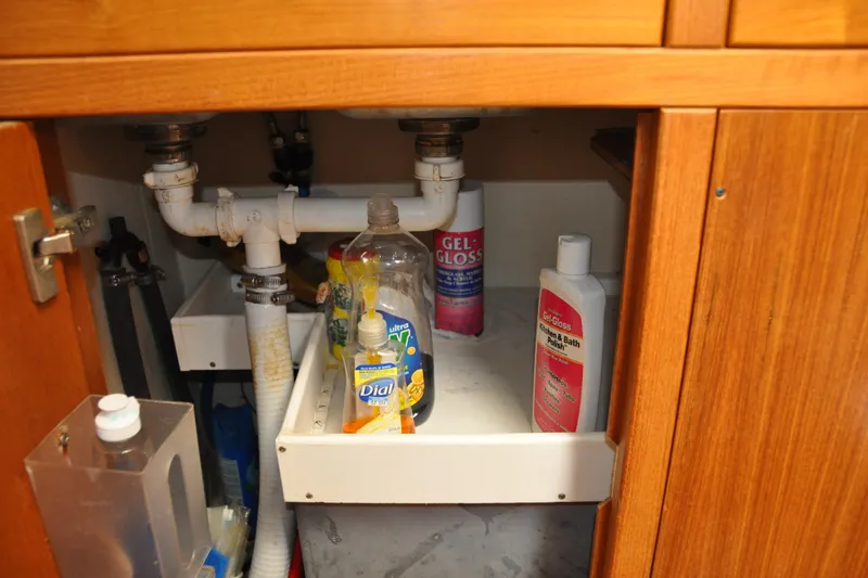 Slide: The Image of Under-sink storage in a 2003 Catalina 387, featuring cleaning supplies and plumbing. - 56