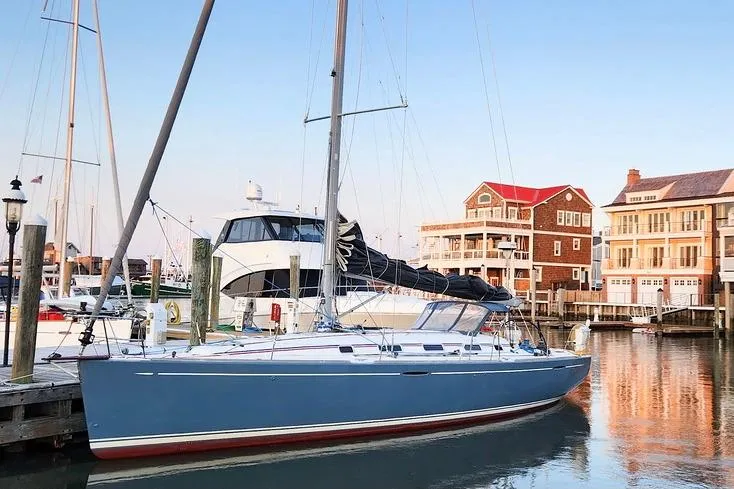 The Image of 2005 Beneteau First 44.7 sailboat docked at a marina with waterfront homes. - 0