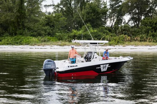 Slide: The Image of 2023 Wellcraft 222 Fisherman boat on calm water near a forested shoreline. - 2