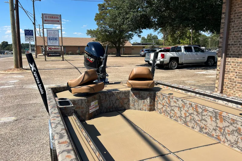Slide: The Image of 2026 Xpress X18DB boat with camo design, parked outdoors near dealership signs. - 2