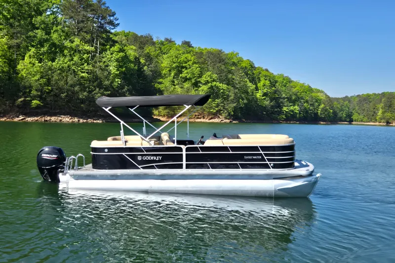 Slide: The Image of 2023 Godfrey Sweetwater 2286 C pontoon boat on a serene lake with lush greenery. - 4