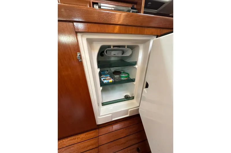 Slide: The Image of Open fridge inside a 2000 Beneteau 50 yacht, showcasing wooden cabinetry and glass shelves. - 82