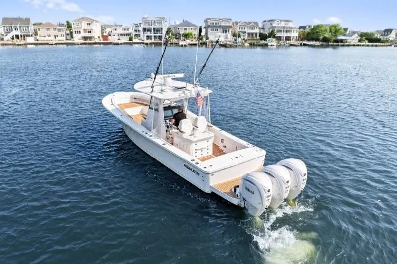 Slide: The Image of 2024 Regulator 34 boat cruising on a calm waterfront with houses in the background. - 2