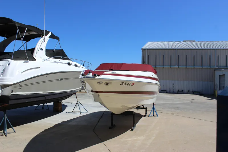 The Image of 2005 Larson LXi 268 boat on stands beside another boat, clear blue sky background. - 1