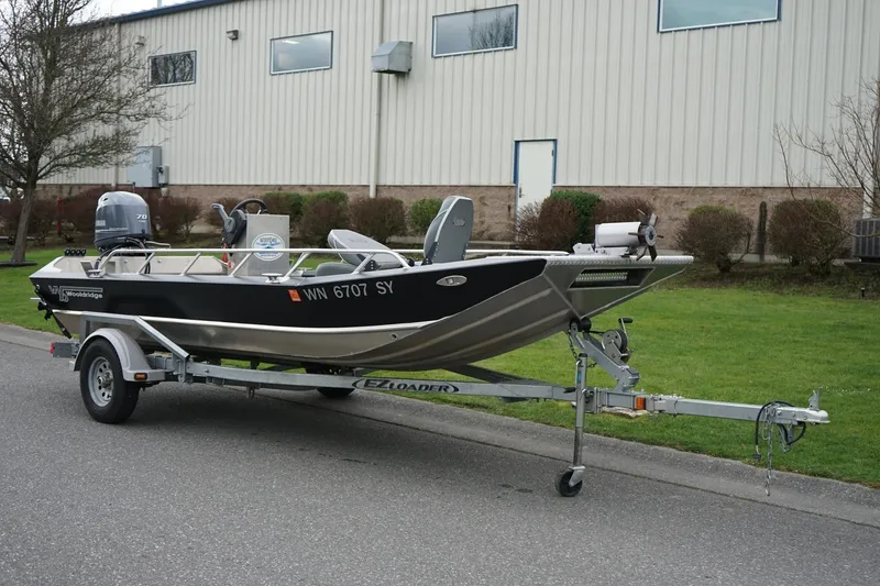 Slide: The Image of 2021 Wooldridge 16 Alaskan LT boat on trailer, parked outdoors near industrial building. - 1