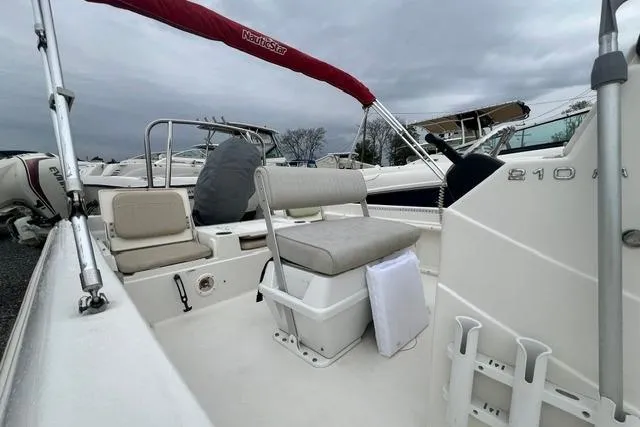 Slide: The Image of 2013 NauticStar 210 Coastal boat interior with seating and canopy under cloudy sky. - 7
