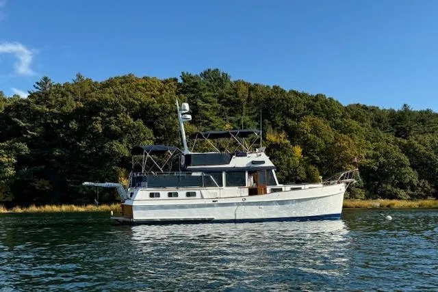 Slide: The Image of 1983 Grand Banks 42 Motoryacht cruising on a serene lake with lush forest backdrop. - 76