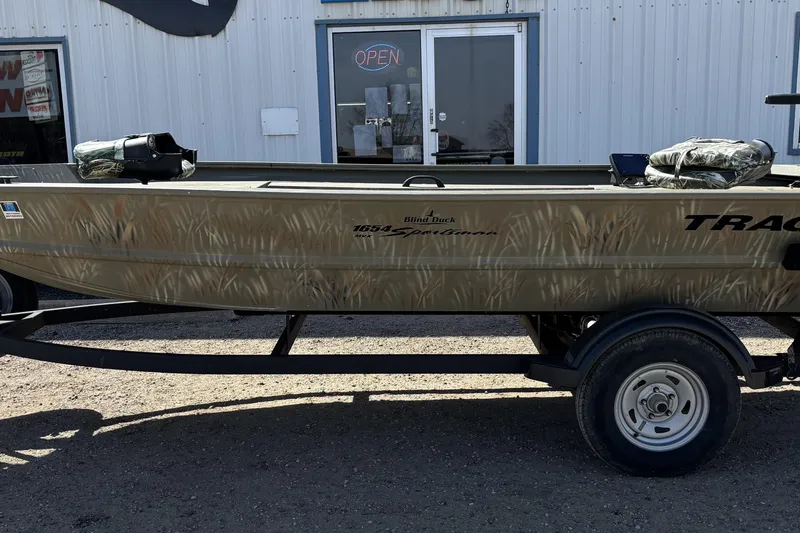 Slide: The Image of 2024 Tracker Grizzly 1654 T Sportsman boat on trailer, parked outside a building. - 2