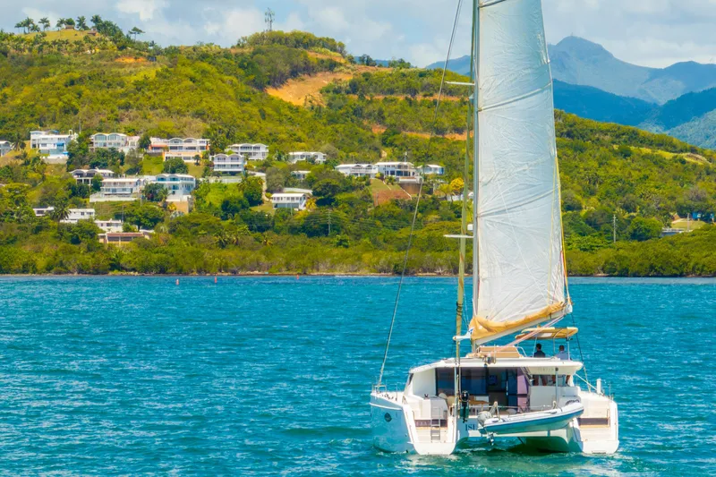 Slide: The Image of Sailing catamaran Fountaine Pajot Helia 44, 2014, on turquoise waters near lush hillside homes. - 2