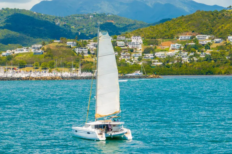 Slide: The Image of 2014 Fountaine Pajot Helia 44 catamaran sailing near scenic coastal hills. - 56