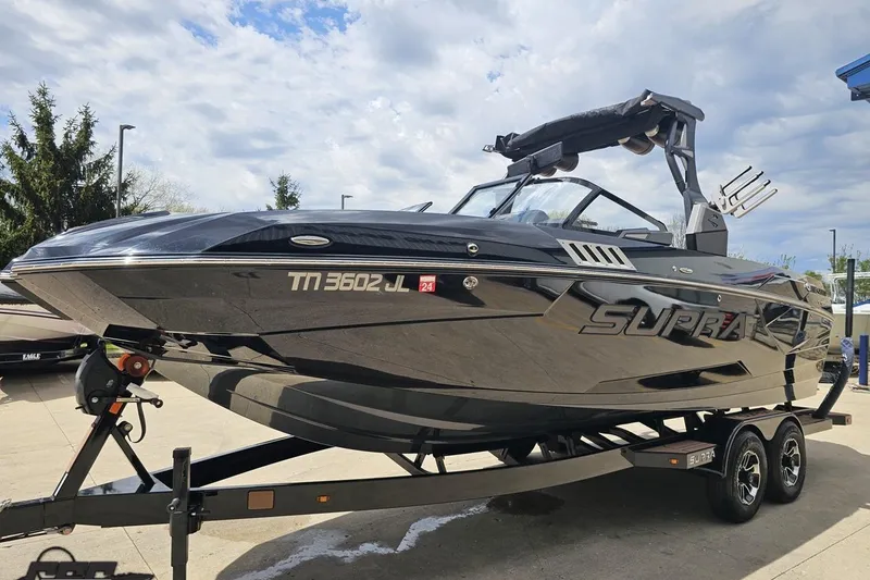 Slide: The Image of 2022 Supra SE 550 boat on trailer, sleek black design, parked outdoors under cloudy sky. - 21