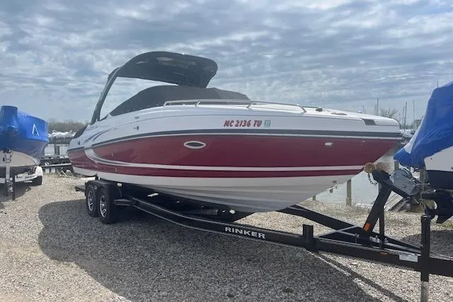 The Image of 2015 Rinker 276 Captiva Cuddy boat on trailer, red and white design, parked outdoors. - 0