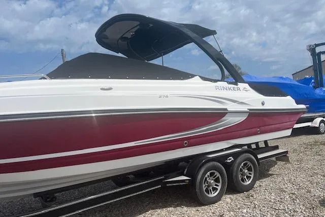 Slide: The Image of 2015 Rinker 276 Captiva Cuddy boat on trailer, featuring sleek red and white design. - 2