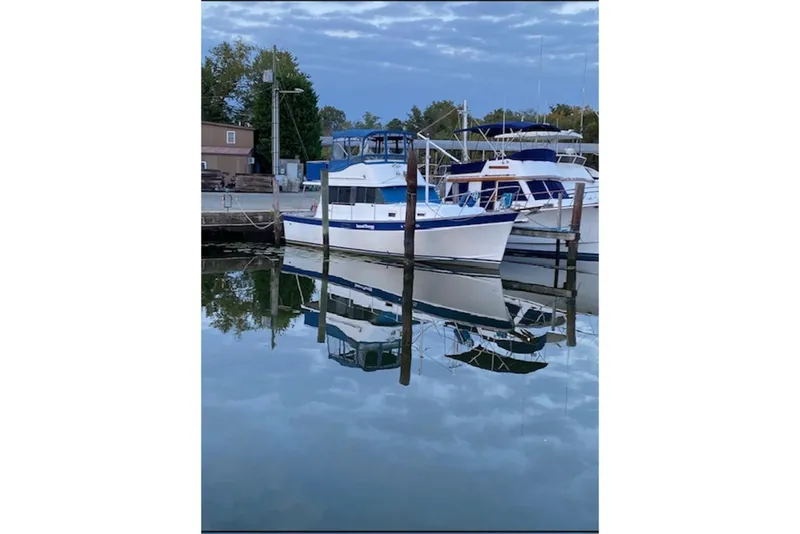 Slide: The Image of 1978 Mainship 34 Trawler docked, reflecting on calm water under a cloudy sky. - 3