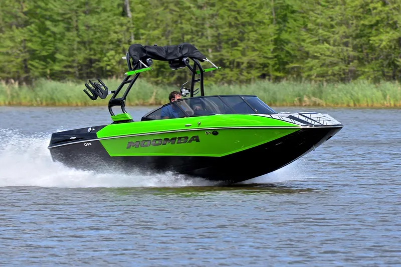 The Image of 2024 Moomba Mondo boat speeding on a lake with lush green surroundings. - 1