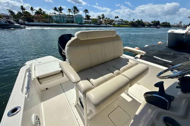Slide: The Image of 2023 Boston Whaler 220 Dauntless boat interior with beige seating, on a sunny waterfront. - 22