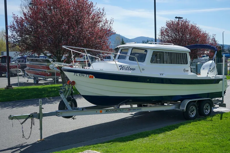 The Image of 2024 C-Dory 23' Venture Sport boat on trailer, parked near trees and mountains. - 1