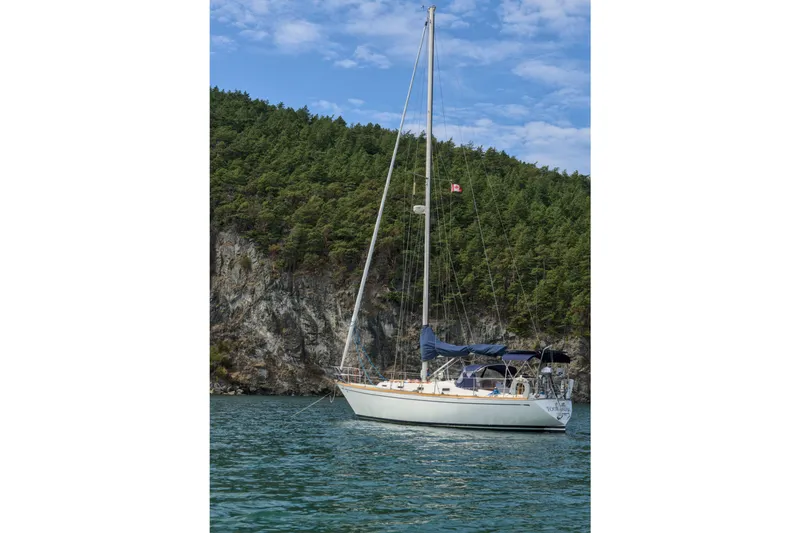 The Image of Sailboat Tartan 37 (1980) anchored near forested cliffs under a blue sky. - 0