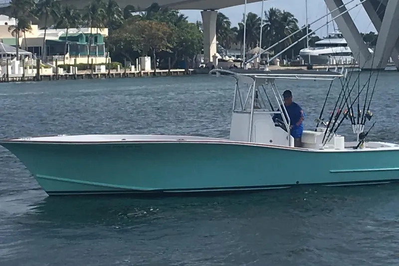 The Image of 1977 Scarborough 27 CC boat in marina, turquoise hull, man at helm, calm water. - 0