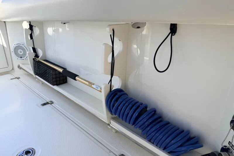 Slide: The Image of Storage compartment on a 2022 Boston Whaler 250 Outrage, featuring a coiled blue hose and accessories. - 23