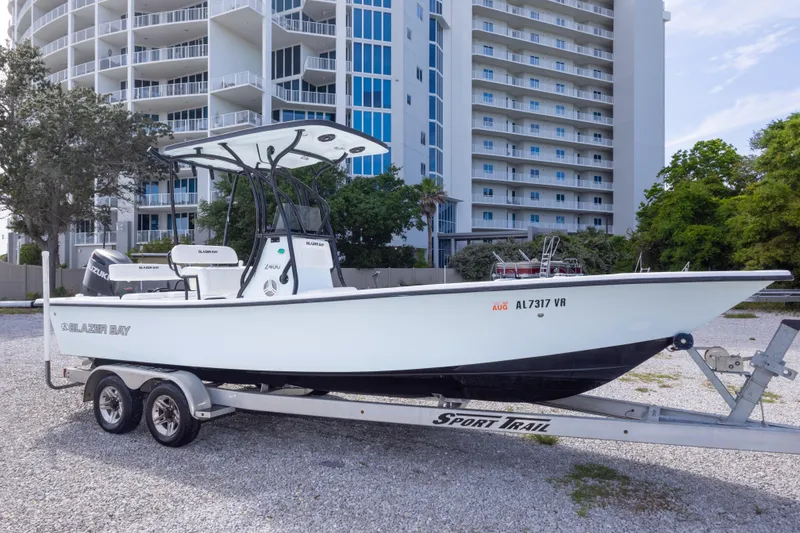 Slide: The Image of 2019 Blazer Bay 2400 boat on trailer, parked near modern high-rise buildings. - 8