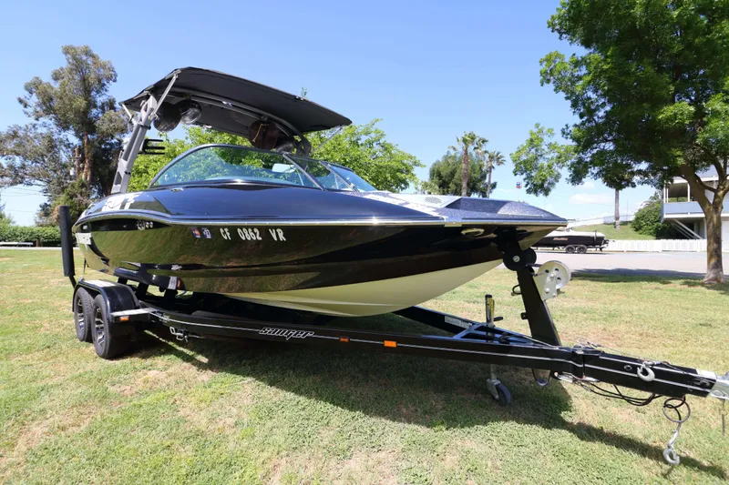 Slide: The Image of 2018 Sanger 212 SL boat on trailer, parked on grass under clear sky. - 4