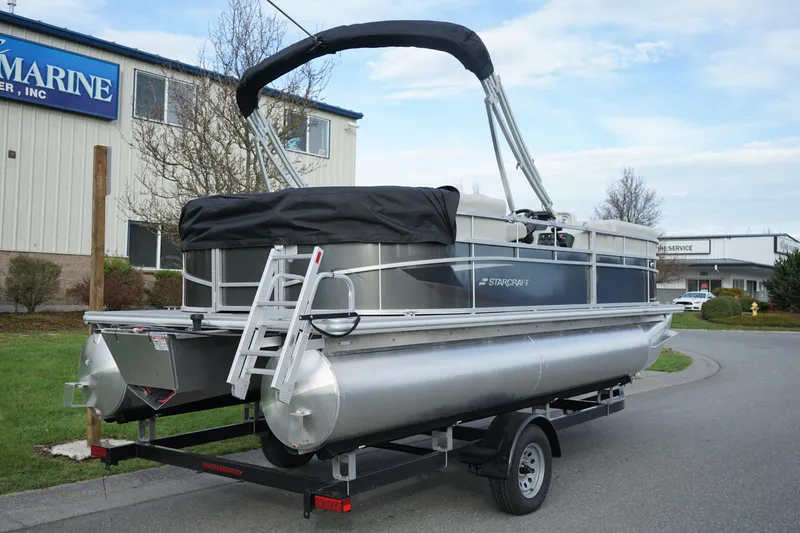 Slide: The Image of 2025 Starcraft LX 16 R pontoon boat on trailer, parked near a building. - 3