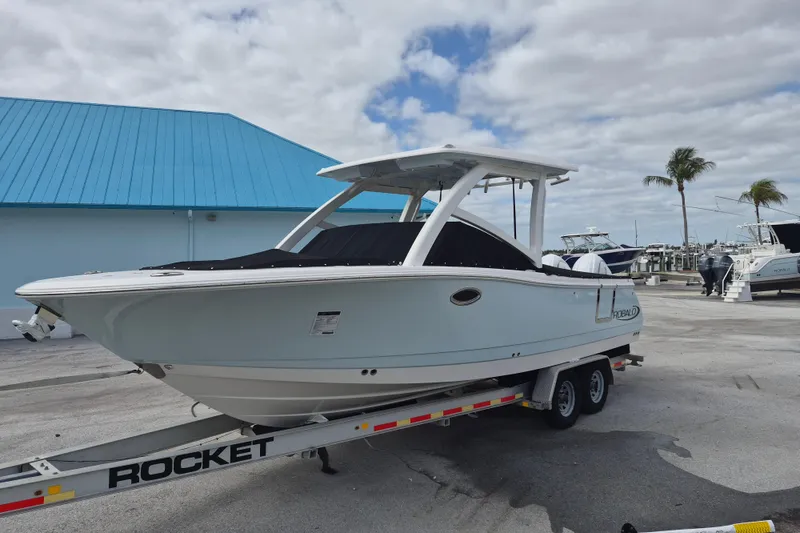 The Image of 2026 Robalo R277 Dual Console boat on trailer, parked outdoors under cloudy sky. - 10